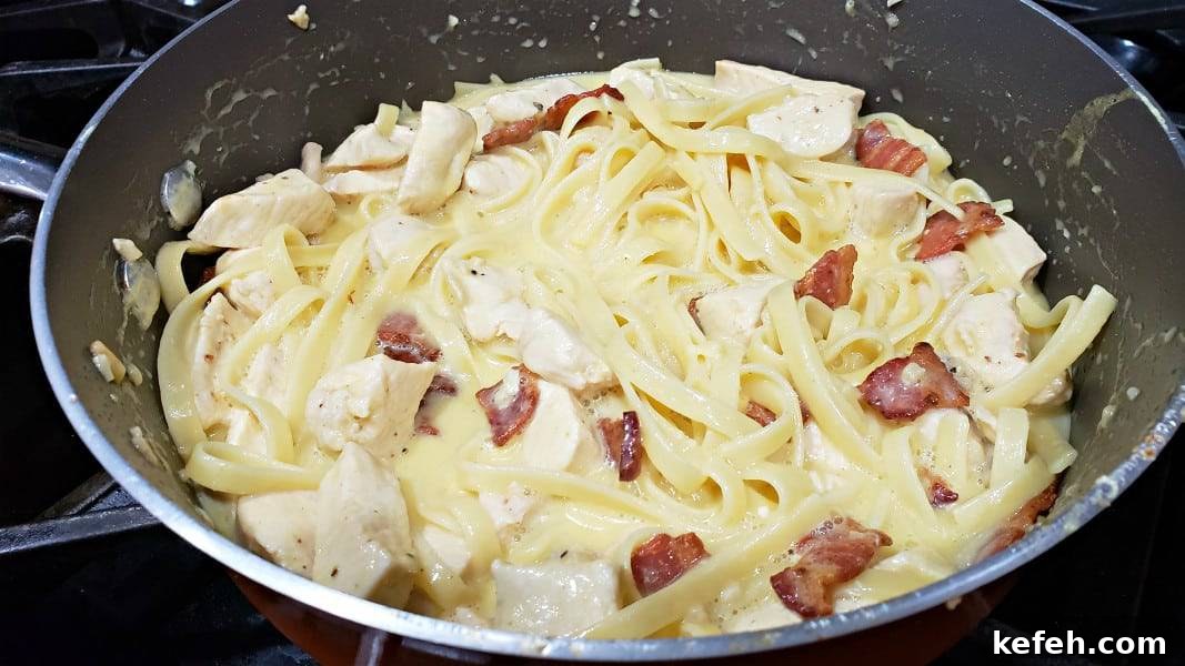 Creamy Bacon and Chicken Carbonara Recipe 7 diced chicken, pasta, bacon, and parmesan sauce cooking in a large pan for this Chicken Carbonara recipe.