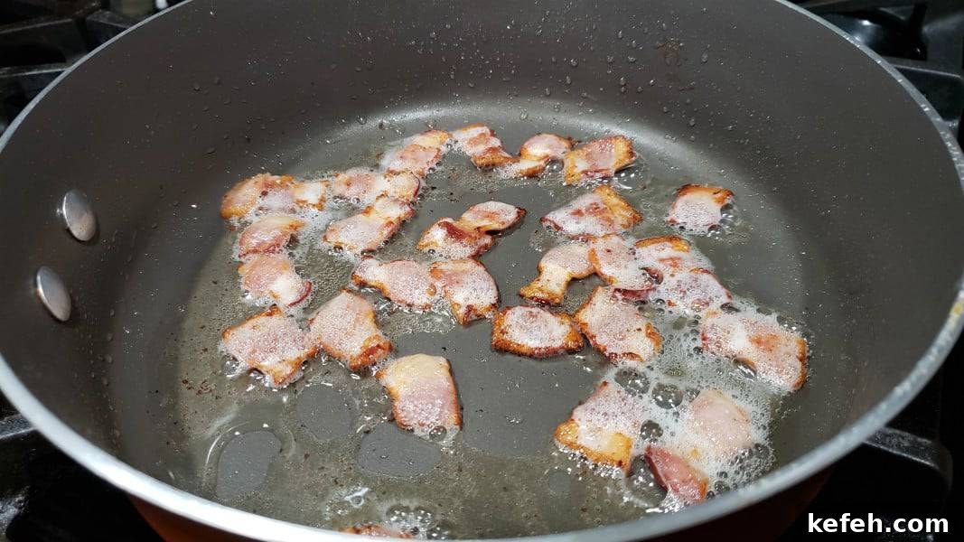Creamy Bacon and Chicken Carbonara Recipe 4 bacon pieces frying in a large pan.