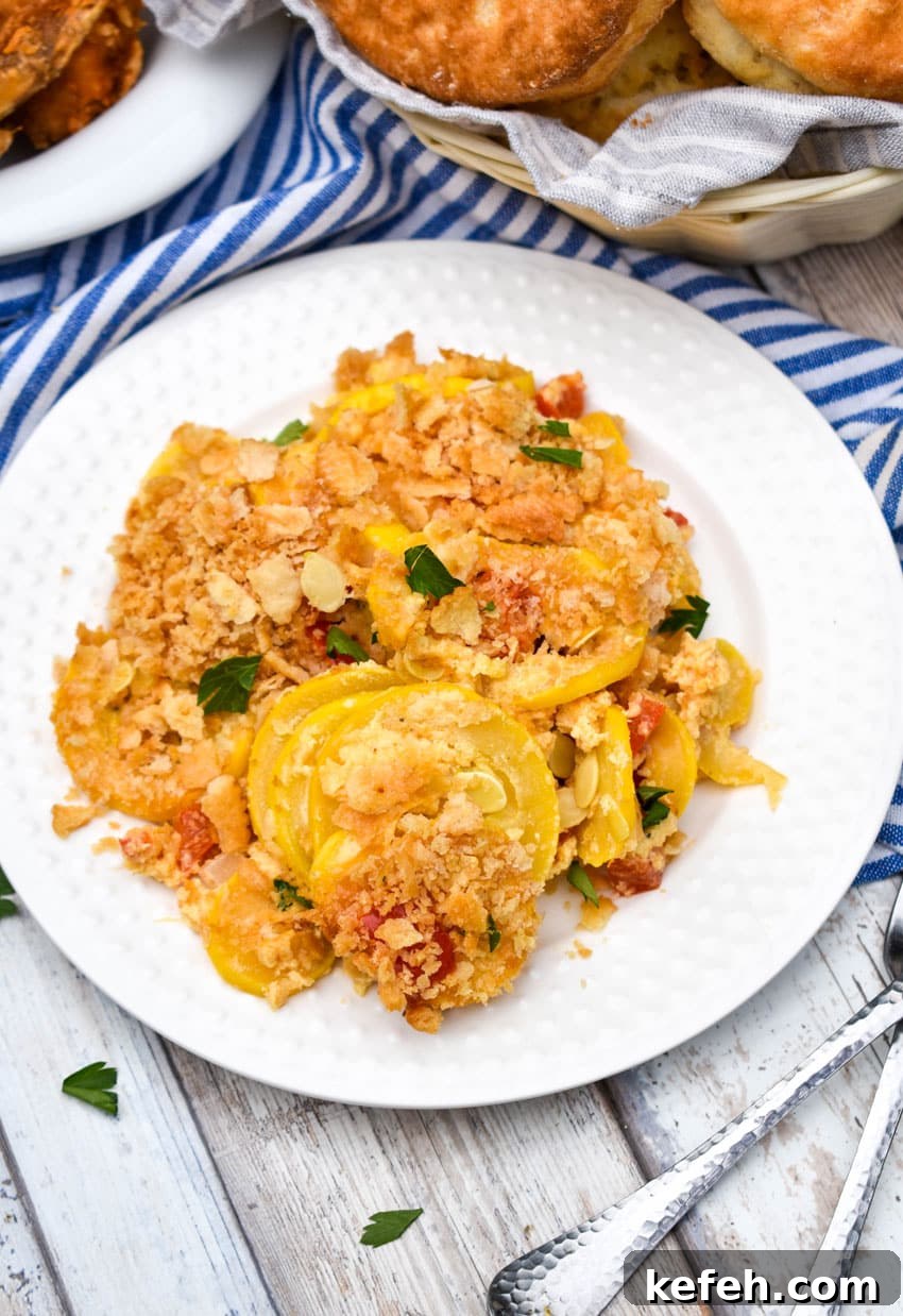 Classic Southern Squash Casserole Recipe for Comforting Dinners 6 southern squash casserole on a small white plate with a basket of biscuits and platter of fried chicken on the side