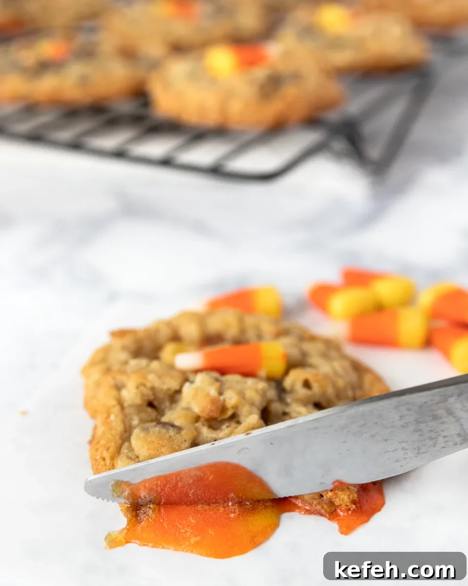 melted candy corn being cut off the edge of a cookie by a table knife