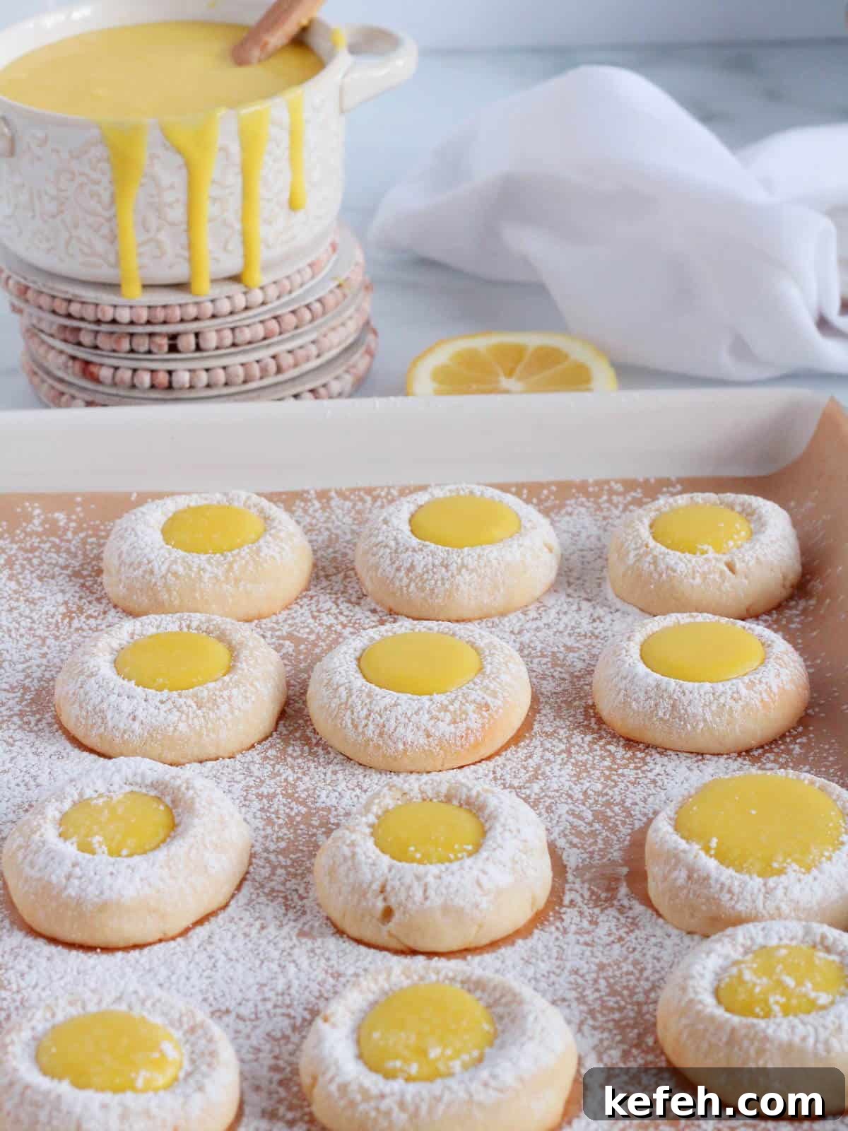 Lemon cookies with lemon curd lined next to each other on baking sheet,with white decoration in the background.