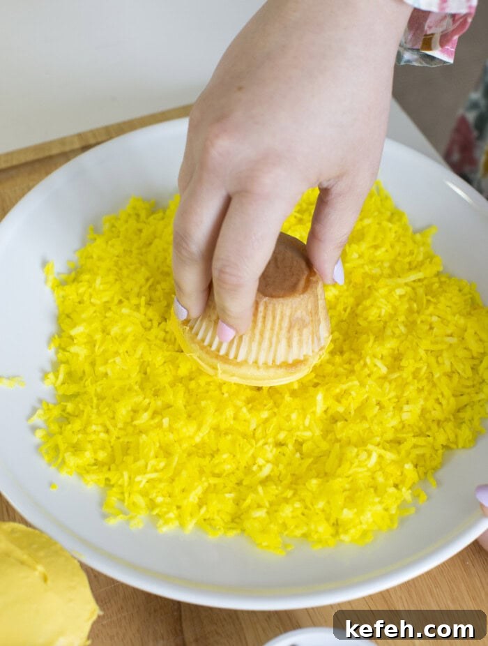 Dipping frosted Easter chick cupcake into a plate of yellow shredded coconut.