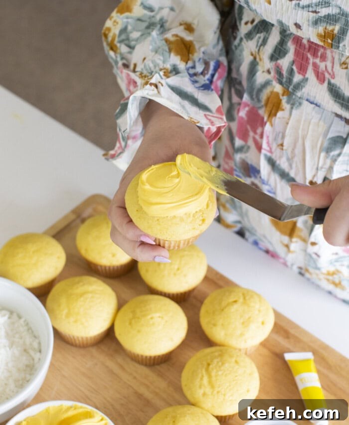 Frosting cupcakes with yellow frosting.