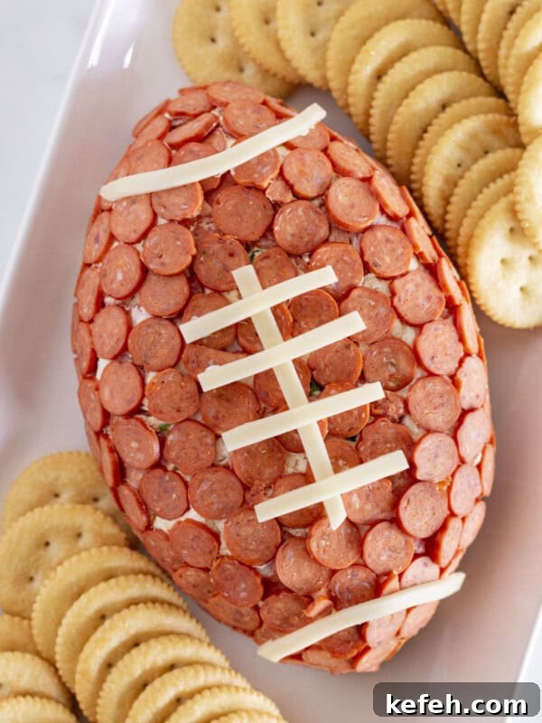 A football pepperoni cheese ball on a white tray with crackers.