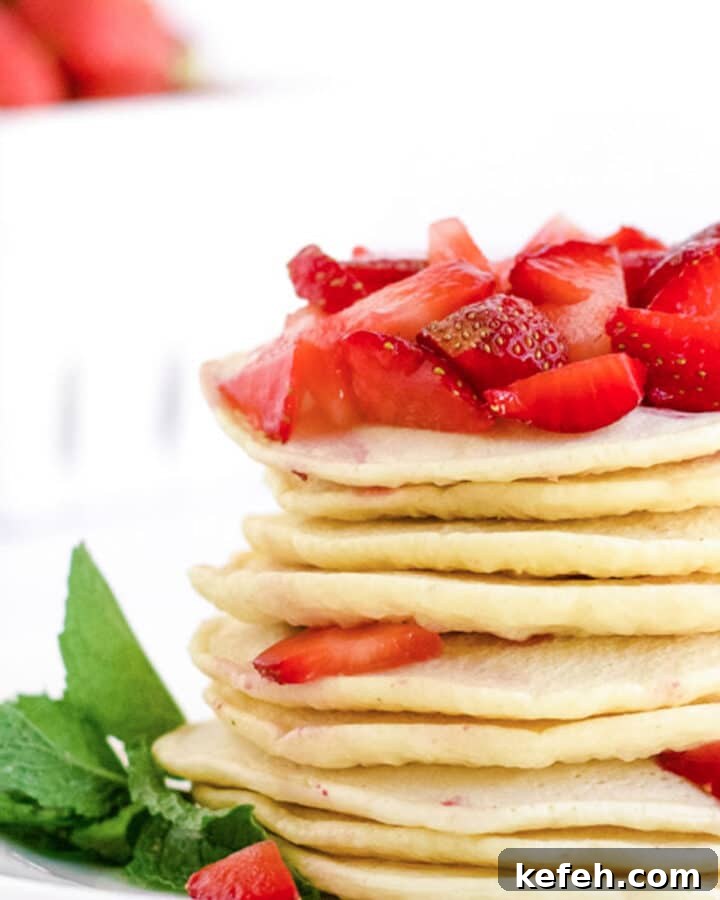 A stack of strawberry pancakes with fresh strawberries on top.