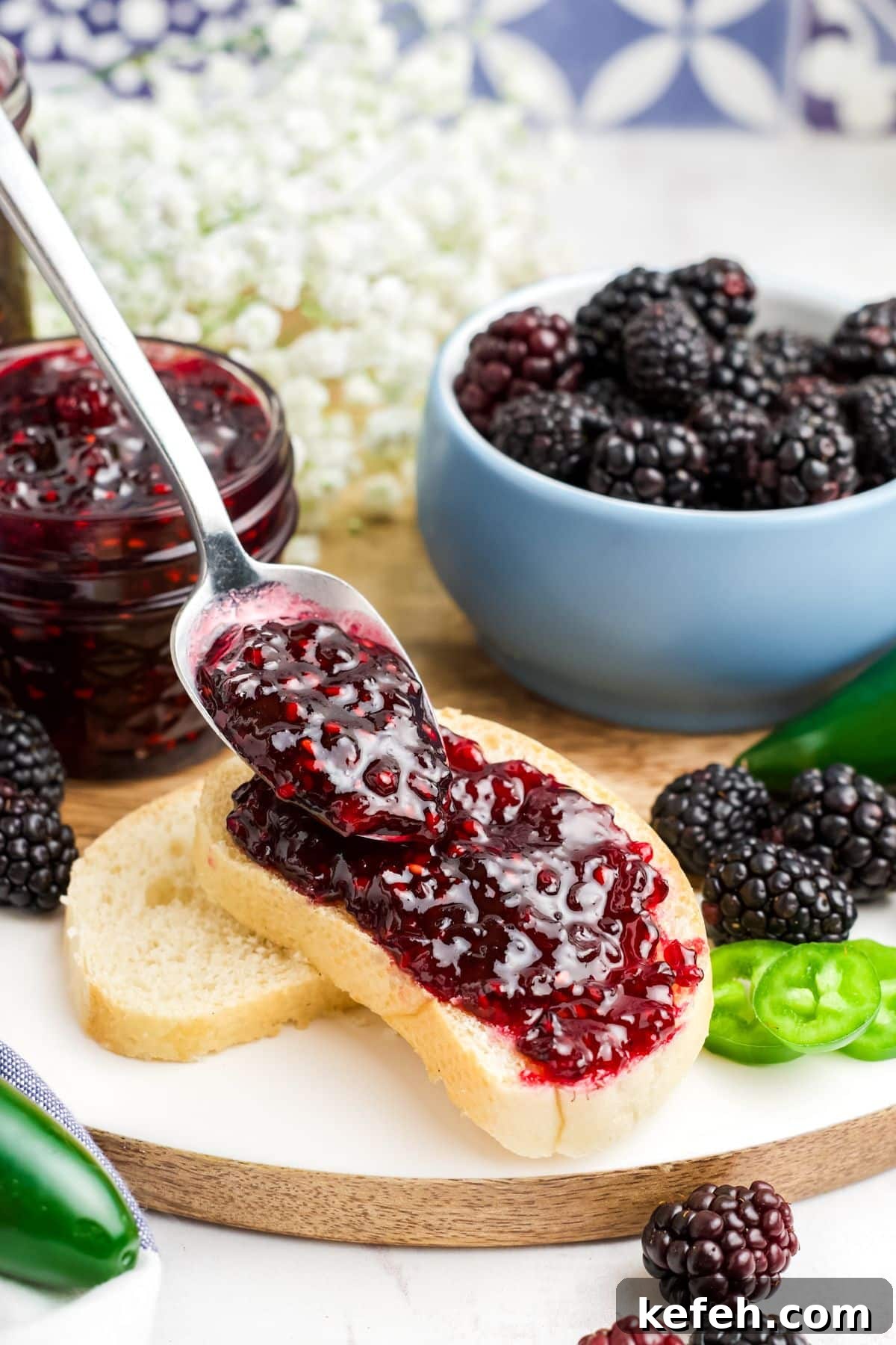 Spicy Blackberry Jalapeño Jam Recipe for Preserving and Gifts 9 A spoon spreading jam on a piece of bread with a jar and bowl of berries in the background.