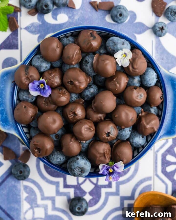 A bowl of chocolate covered blueberries and plain blueberries in a blue bowl together.