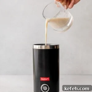 A person preparing a London Fog drink by pouring milk into a coffee maker.