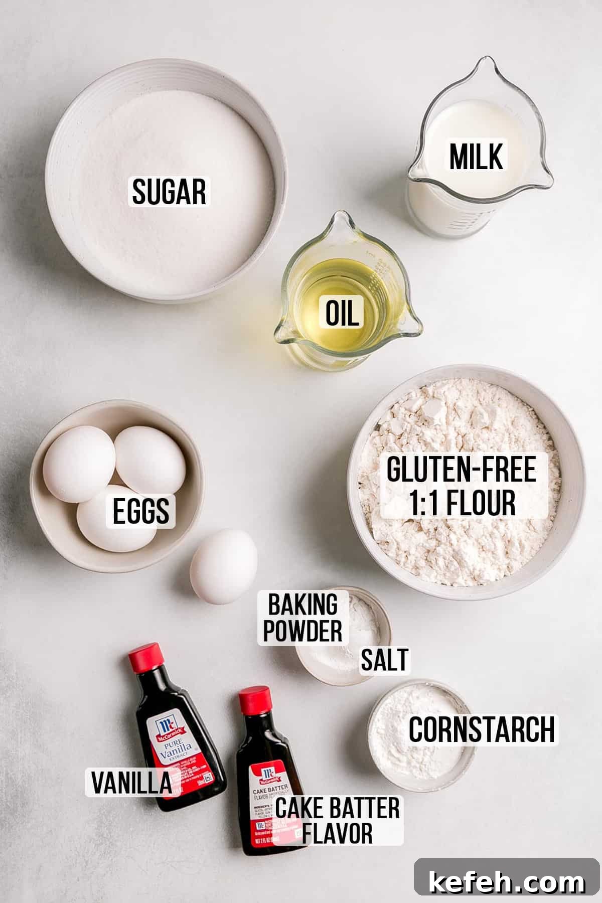 Ingredients for gluten-free yellow vanilla cake measured in bowls on white surface.