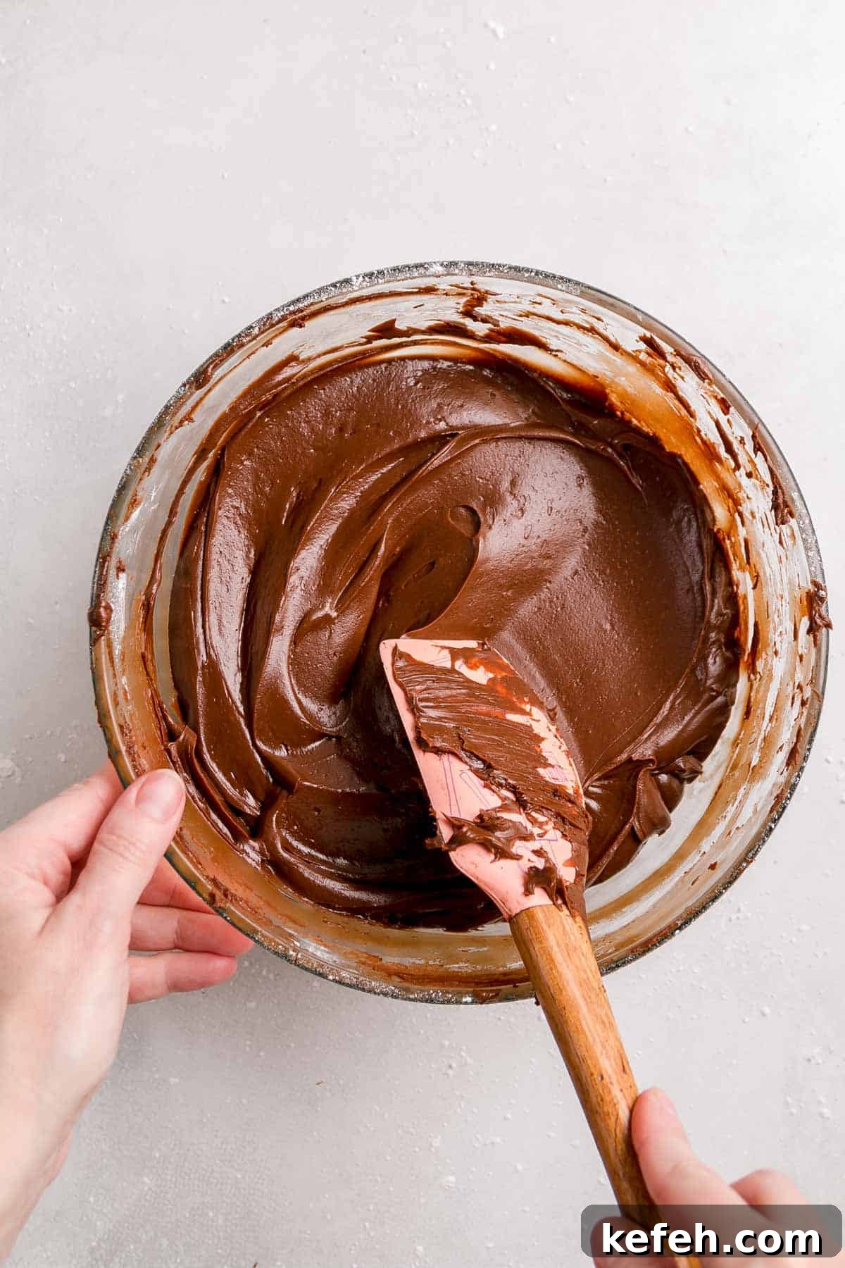 Gluten-free chocolate sour cream frosting in large bowl smoothed with spatula.