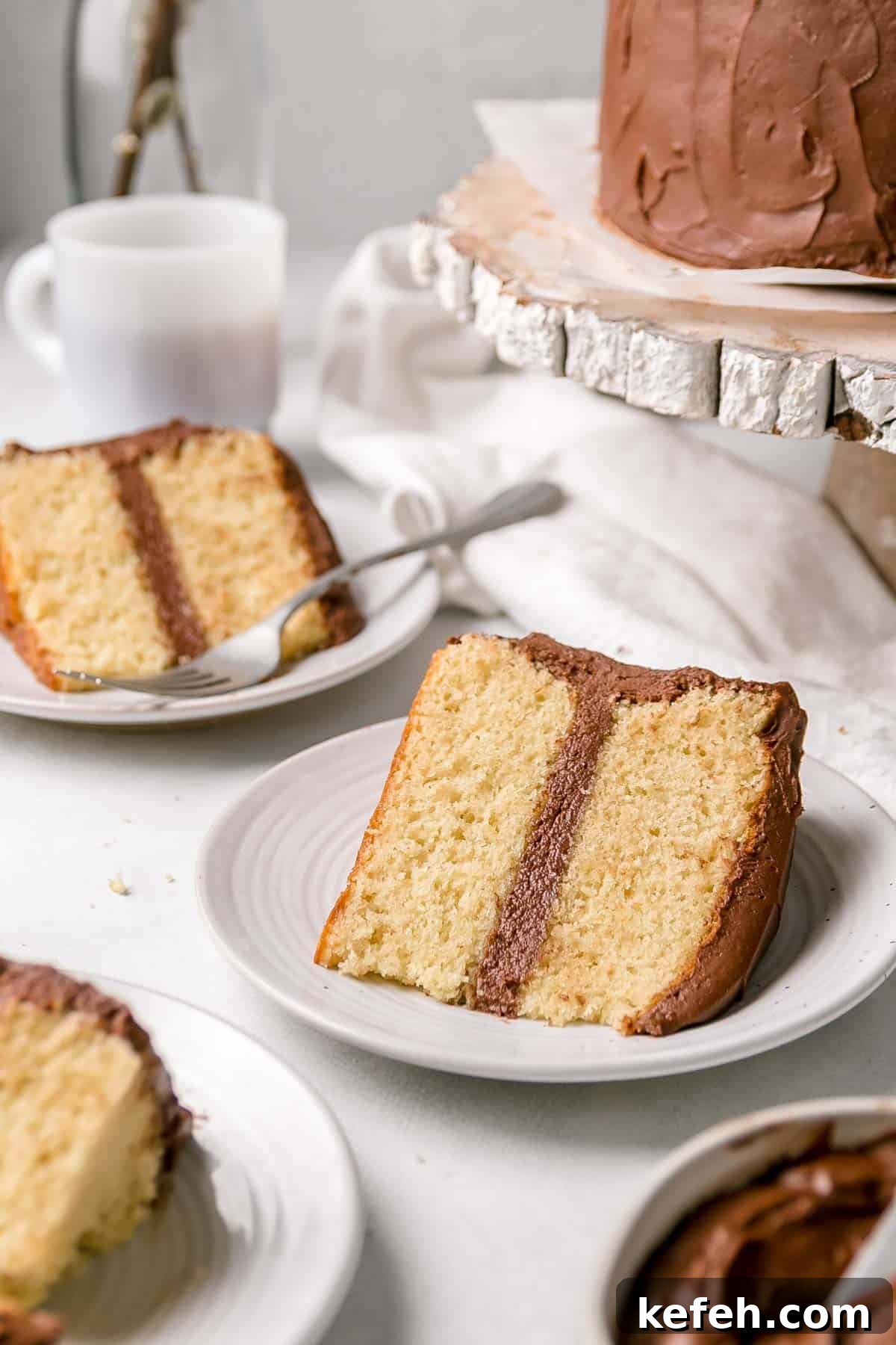 A slice of gluten free yellow cake with chocolate frosting on a small white plate.