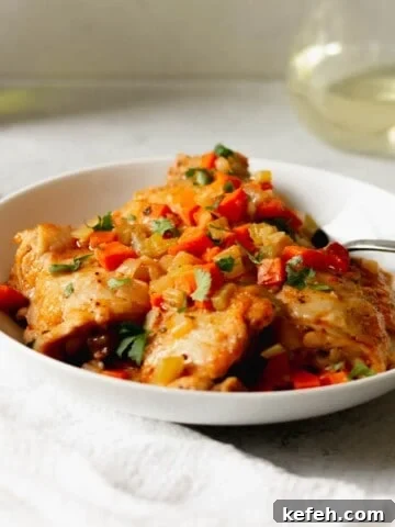 Chicken osso buco in a white bowl in front of a glass of white wine.