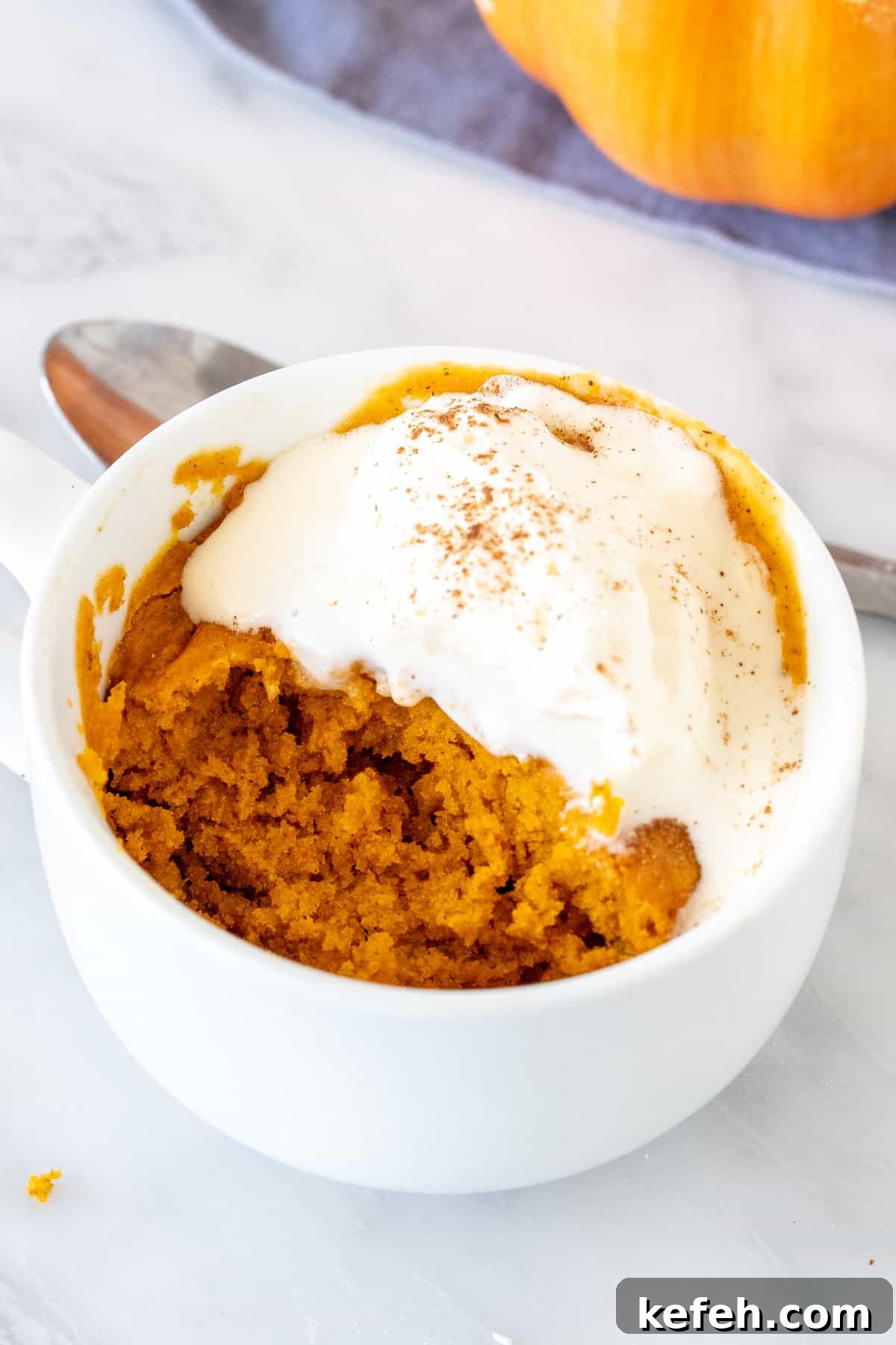 Pumpkin cake in a mug, with a bite taken out and topped with melted whipped cream