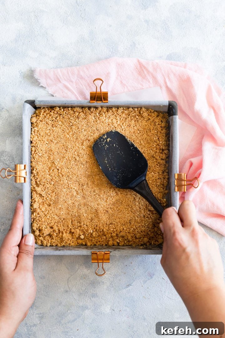 top view of a person pressing biscuit base into baking tin with spatula