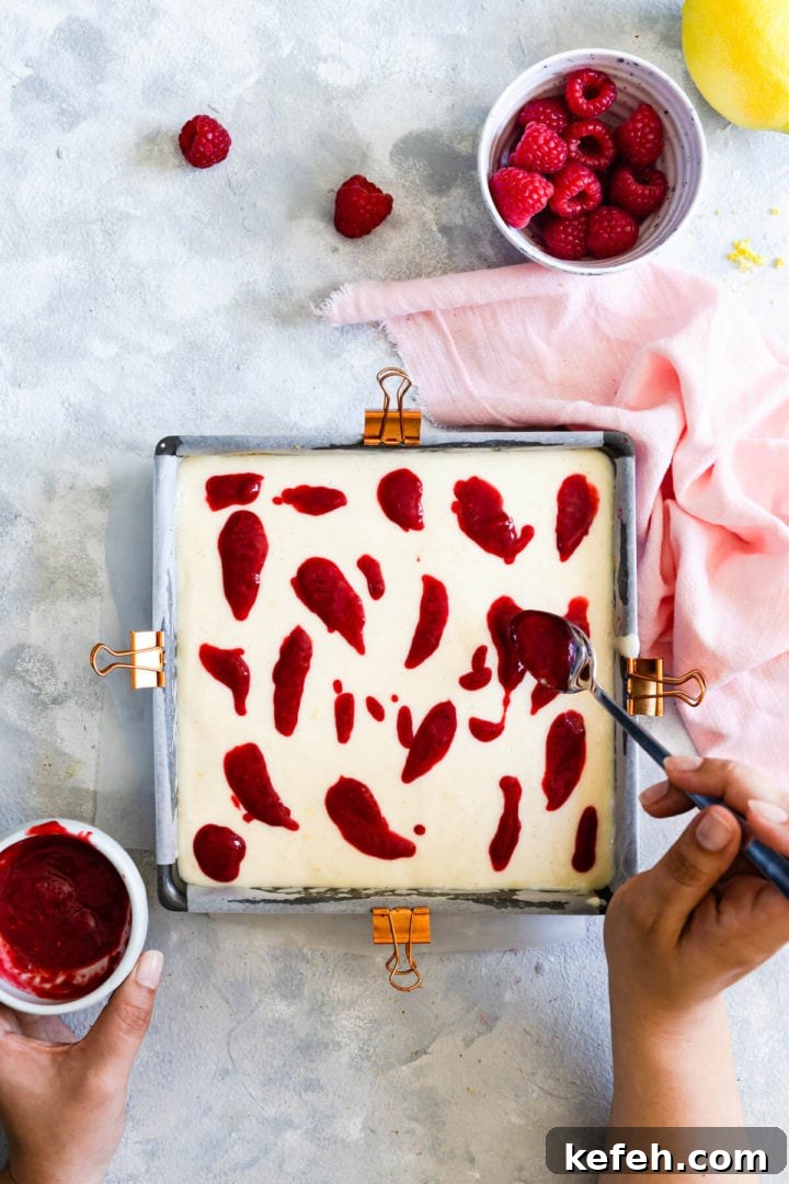 overhead view of a person adding raspberry sauce on top of cheesecake batter