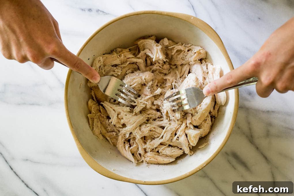 A woman shredding chicken in a bowl with forks.
