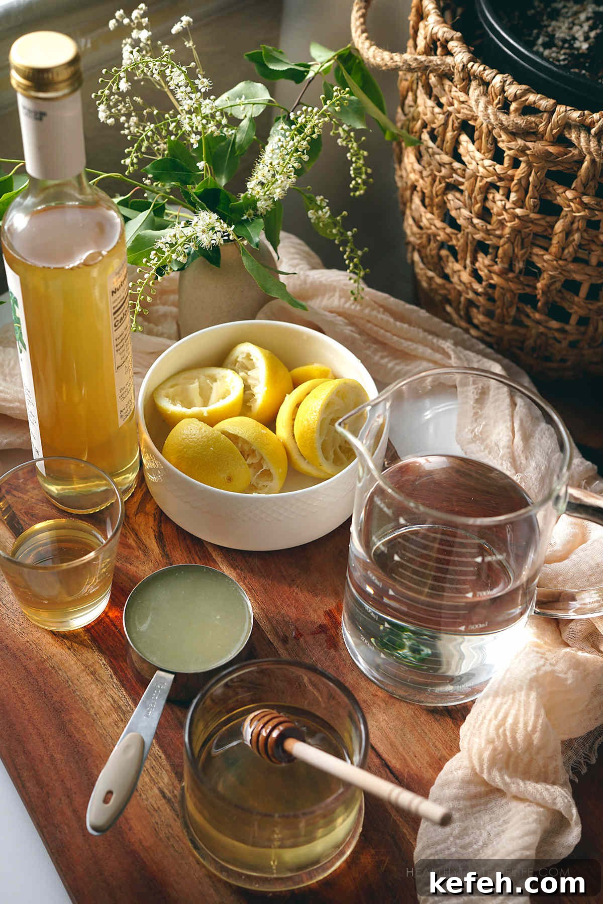 Picture showing the measured ingredients needed for making this homemade elderflower lemonade displayed on a table: elderflower syrup, lemon juice, water and honey.