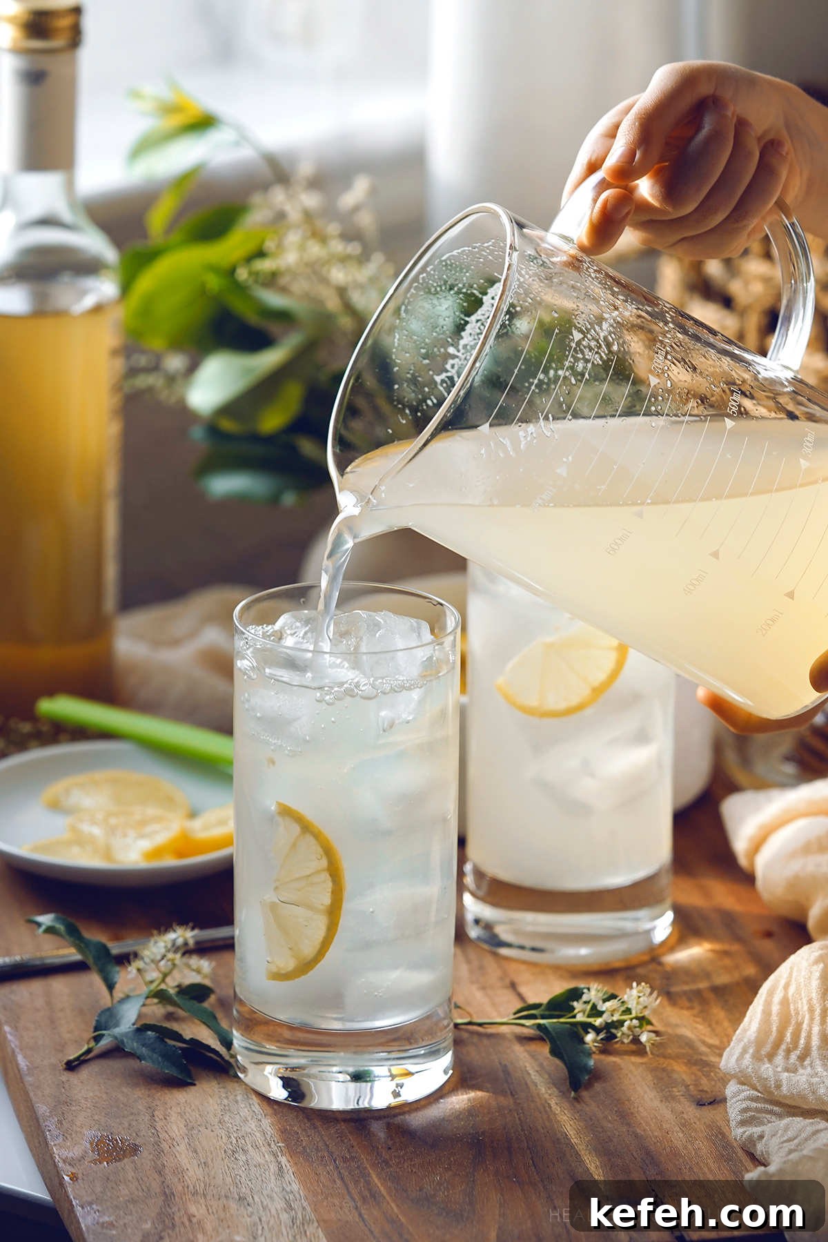 Pouring the mixed elderflower lemonade from a pitcher into serving glasses with ice and garnishes.