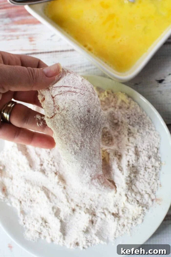 Hand dipping chicken fillet in flour, with beaten eggs nearby, this process mirrors the initial steps of learning how to make chicken tenders.
