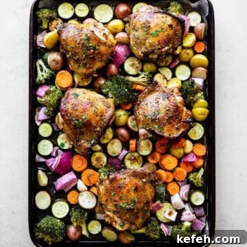 chicken thighs on a bed of veggies on top of a baking sheet