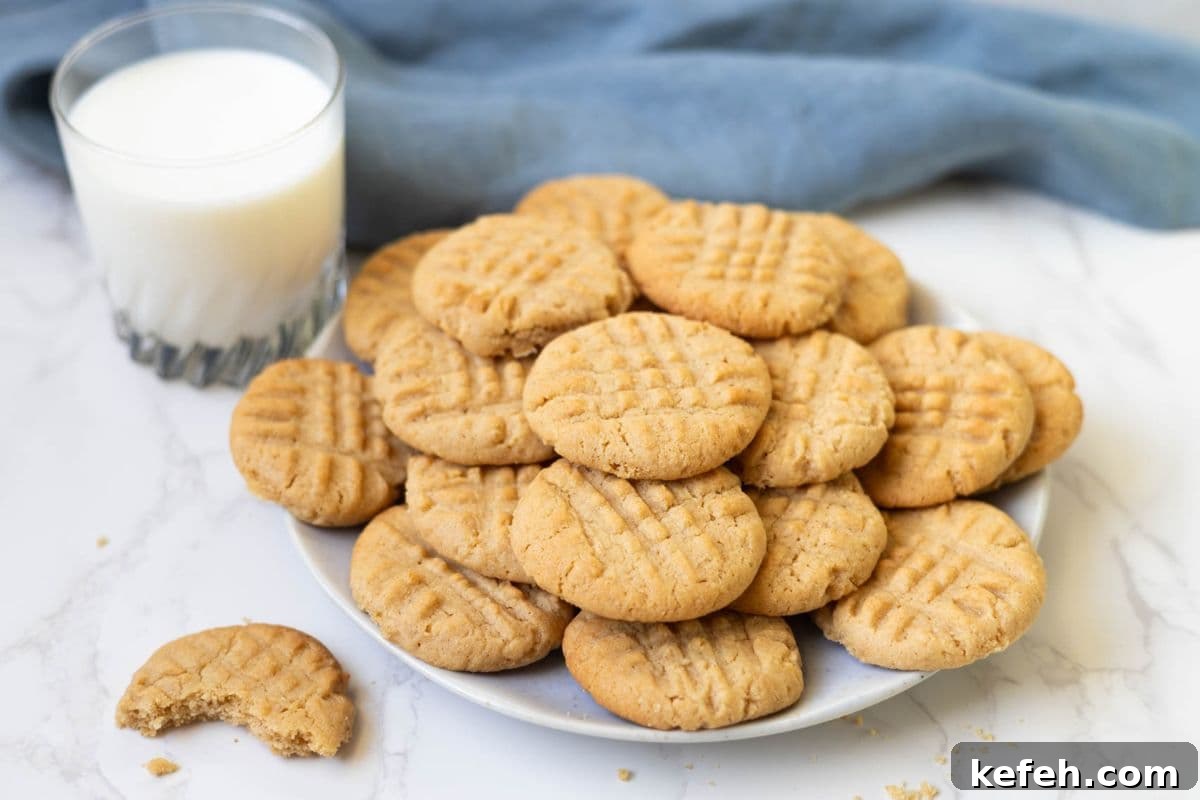 Plate piled high with sourdough peanut butter cookies served with a glass of milk and a partially eaten cookie on the side.