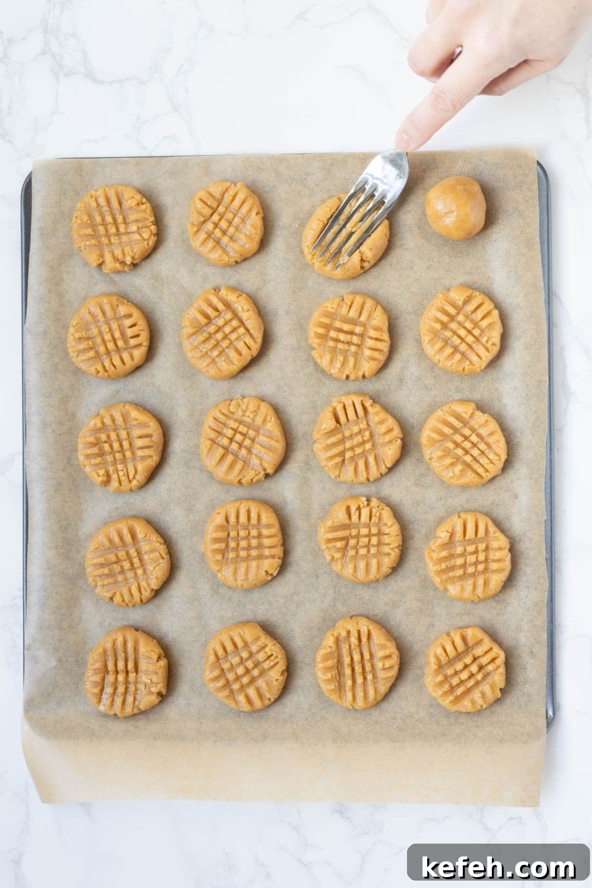 Peanut butter cookie dough balls pressed with a fork on a parchment-lined baking sheet before baking.