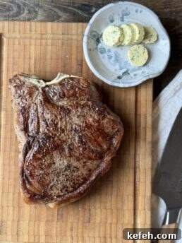 cooked t-bone on wood cutting board with a small plate of sliced herb butter next to a chef knife