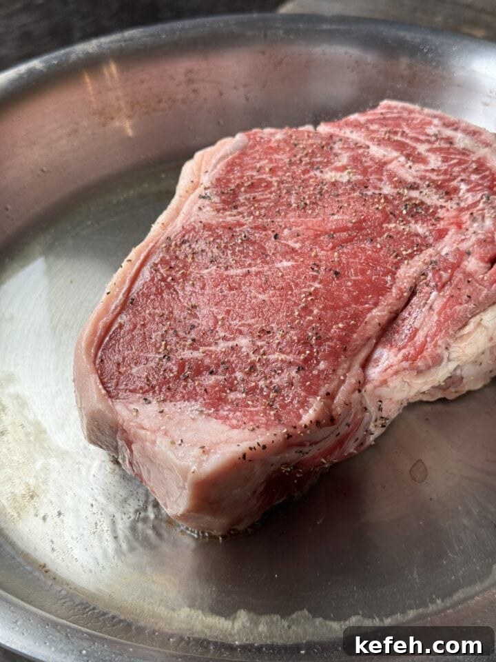 T-Bone Steak Recipe with Garlic Butter and Herbs 4 Juicy raw steak seasoned with salt and pepper on stainless steel tray for cooking.