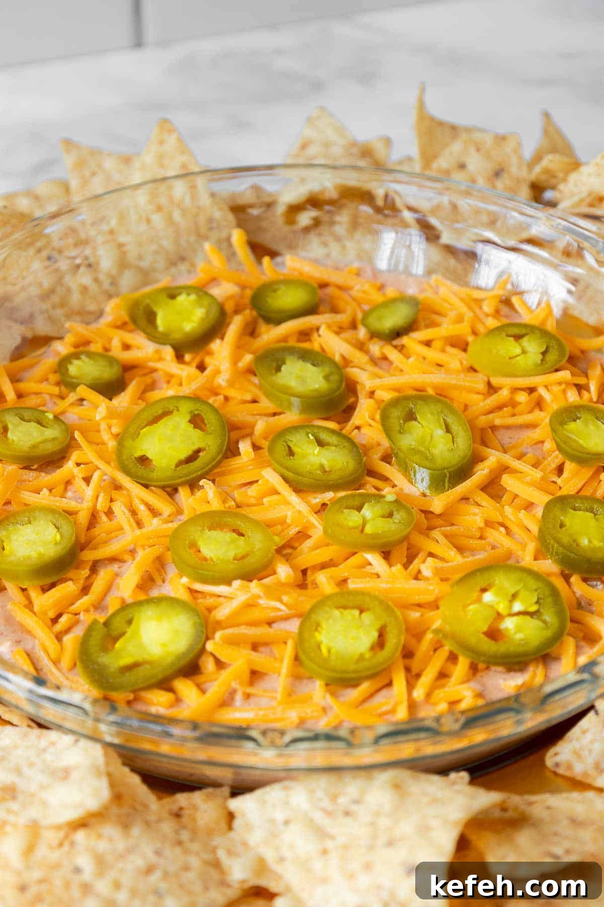 Cream Cheese Salsa Dip Recipe for Parties and Game Day 2 A glass pie dish filled with cream cheese and salsa dip, topped with shredded cheddar cheese and sliced jalapeños, surrounded by tortilla chips.