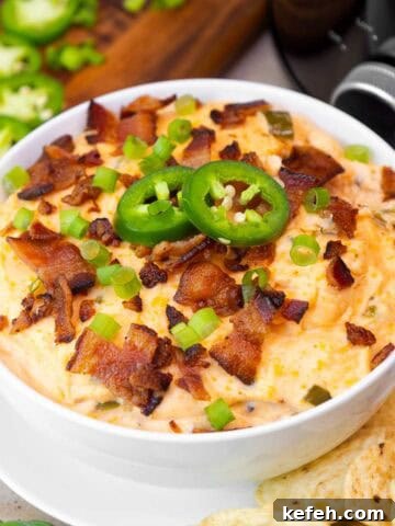 Small bowl of creamy crockpot jalapeño popper dip topped with crispy bacon, sliced jalapeños, and green onions.