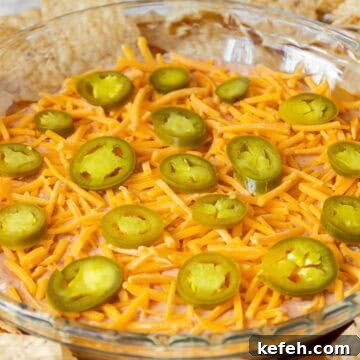 Cream Cheese Salsa Dip Recipe for Parties and Game Day 10 A glass pie dish filled with cream cheese and salsa dip, topped with shredded cheddar cheese and sliced jalapeños, surrounded by tortilla chips.