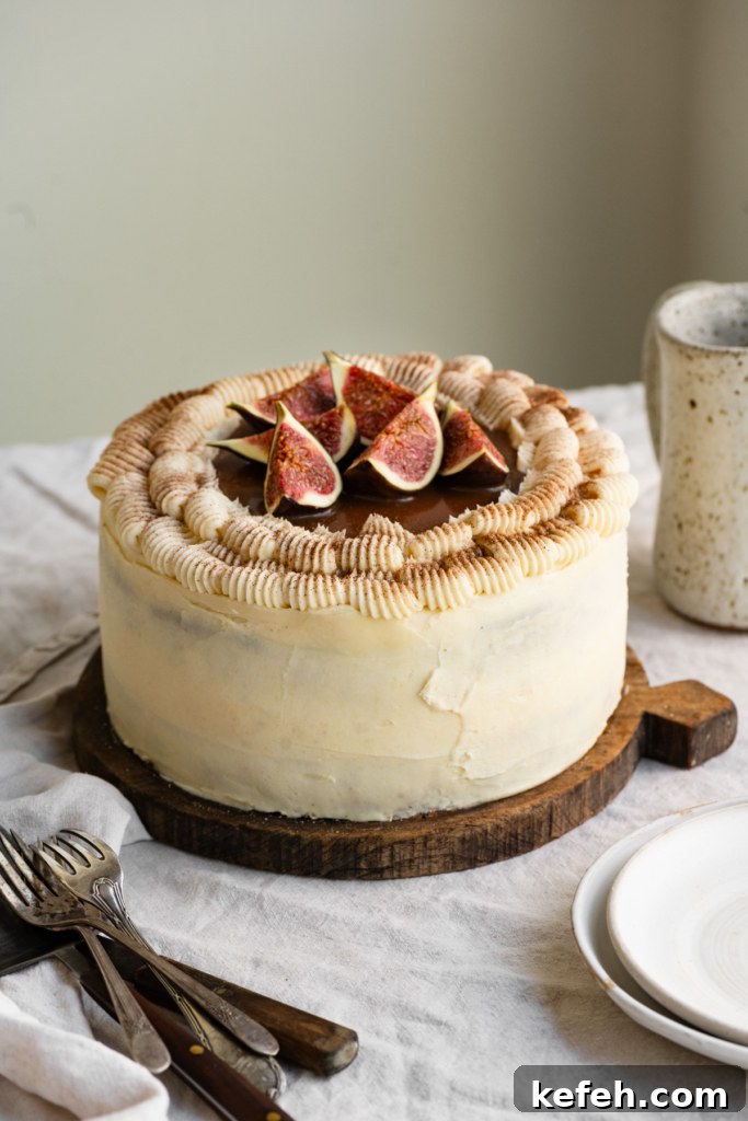 Warm Caramel Apple Spice Cake Recipe 4 Frosted cake topped with caramel sauce and sliced figs on a linen covered table. next to plates and silverware.