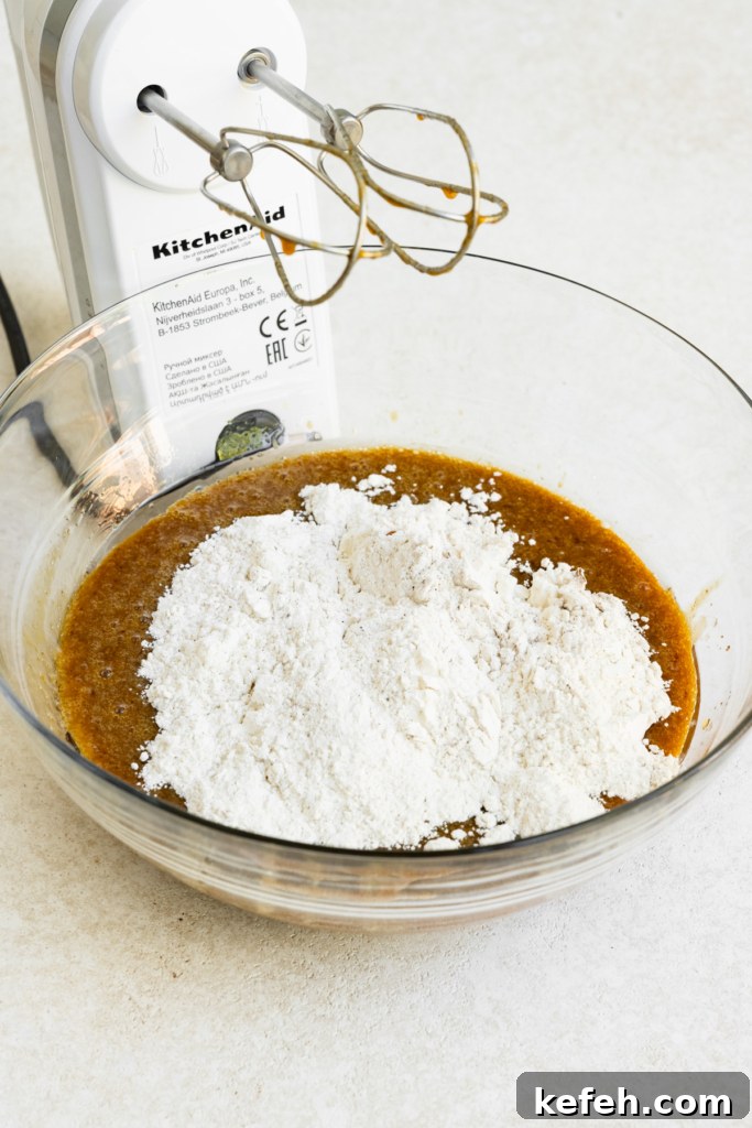 Warm Caramel Apple Spice Cake Recipe 6 Flour mixture on top of wet mixture in a bowl next to a hand mixer.