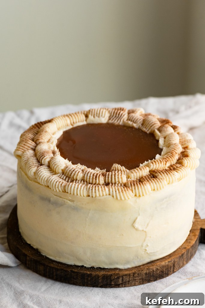 Warm Caramel Apple Spice Cake Recipe 10 Frosted cake topped with caramel sauce sitting on a wood cutting board on a table.