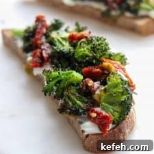 An open sandwich with ricotta cheese, broccoli and sun-dried tomatoes on a plate