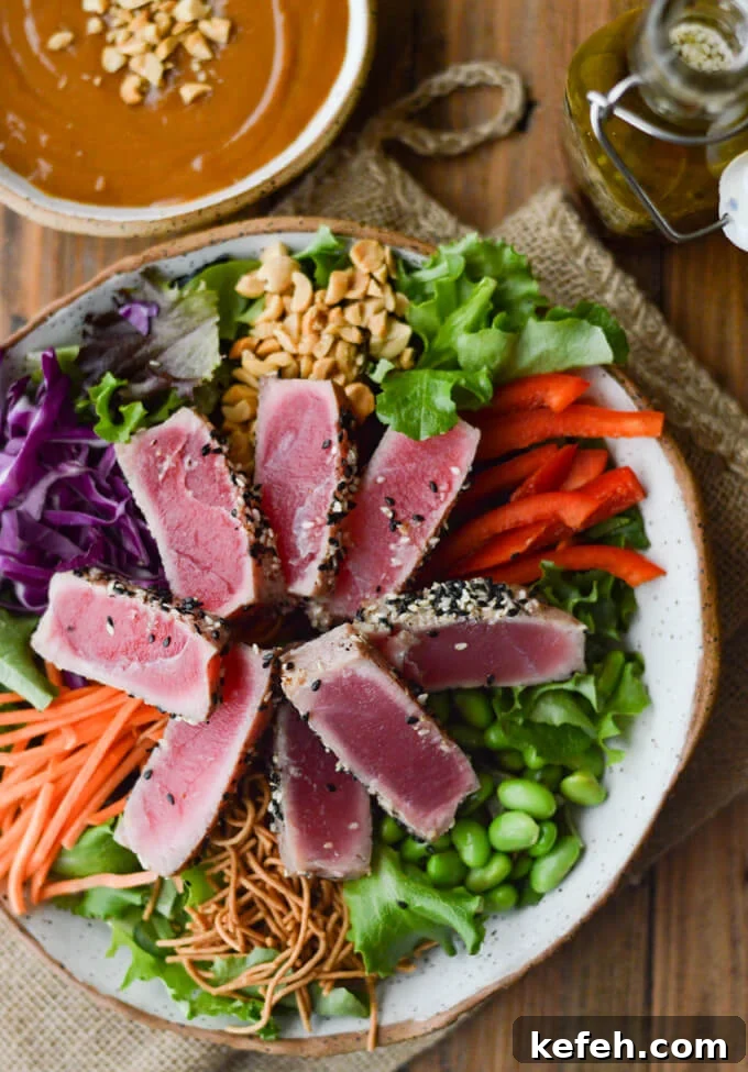 Spicy Peanut Ahi Tuna Salad with Sesame Ginger Dressing 2 A bowl of salad with seared tuna, edamame, red cabbage, peanuts, red peppers and rice noodles with a bowl of peanut sauce next to it.