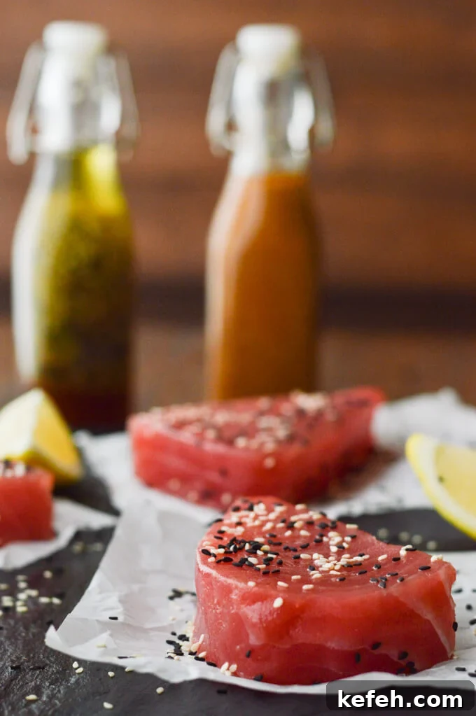 Spicy Peanut Ahi Tuna Salad with Sesame Ginger Dressing 4 3 uncooked ahi tuna steaks on parchments paper with lemon wedges around. A bottle of Asian vinaigrette and a bottle of peanut sauce are in the background.