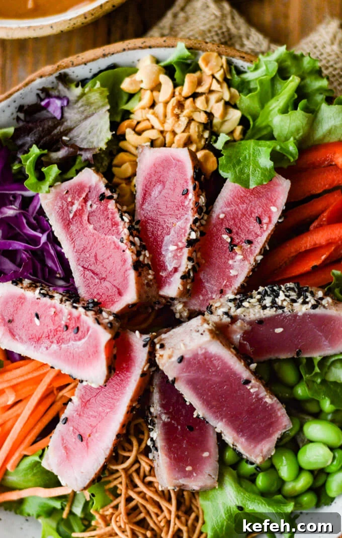 Spicy Peanut Ahi Tuna Salad with Sesame Ginger Dressing 6 A bowl of salad with seared tuna, edamame, red cabbage, peanuts, red peppers and rice noodles with a bowl of peanut sauce next to it.