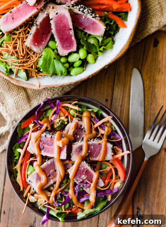 Spicy Peanut Ahi Tuna Salad with Sesame Ginger Dressing 9 An asian salad with seared ahi tuna on top and peanut sauce drizzled on top. Another bowl of salad next to it with a knife and a fork.