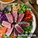 An asian salad with seared ahi tuna on top and peanut sauce drizzled on top.