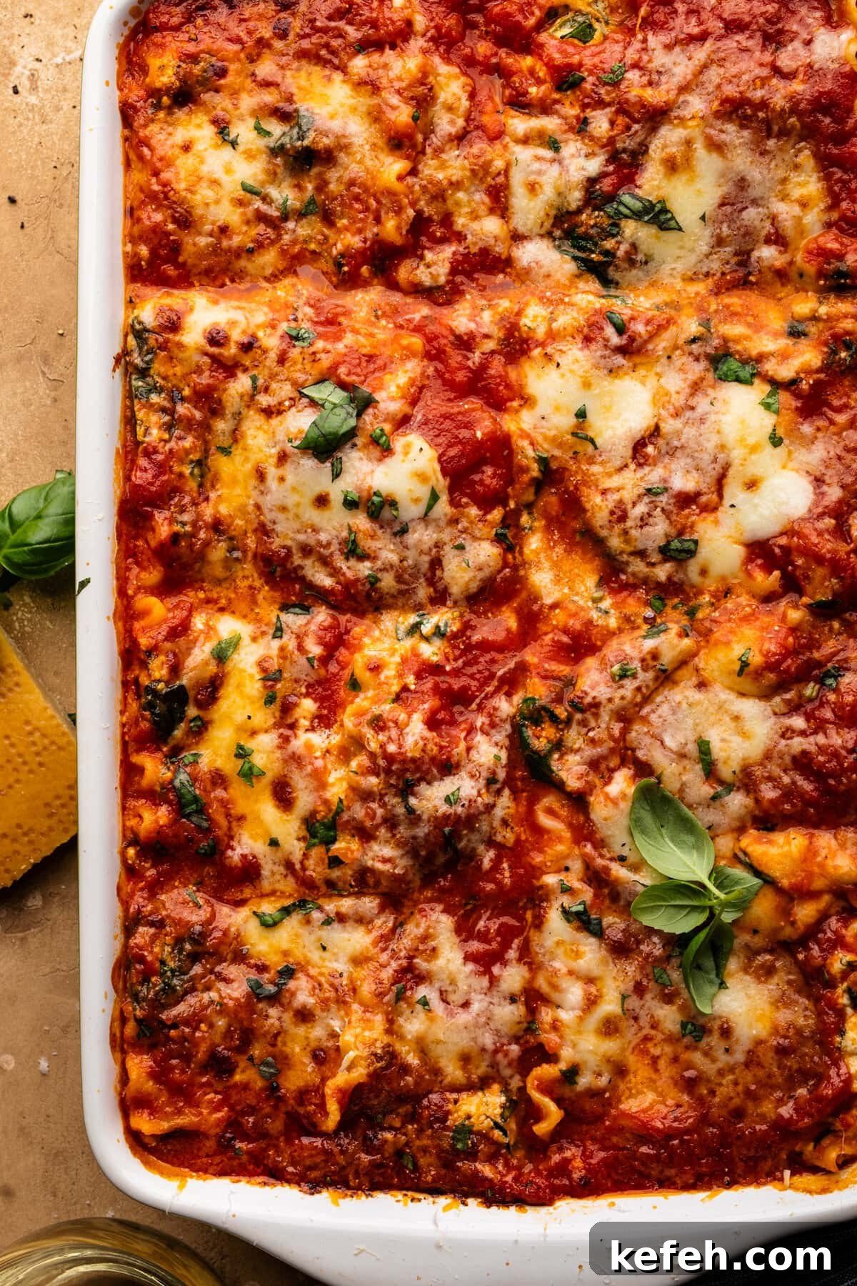Creamy Classic Spinach Lasagna Recipe for Dinner 7 A close-up of lasagna in a white dish. The lasagna has green herbs sprinkled over it and the dish is sitting on a tan background.