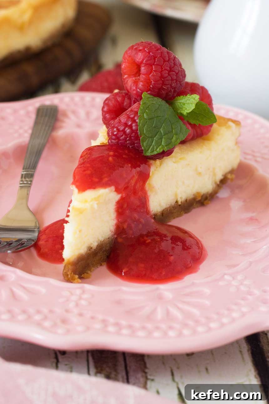 closeup of a piece of White chocolate baked cheesecake with raspberry coulis on a pink plate and with a fork