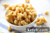 A white bowl of caramel corn puffs sitting on top of a white and blue striped kitchen towel with candied corn puffs surrounding the bowls.