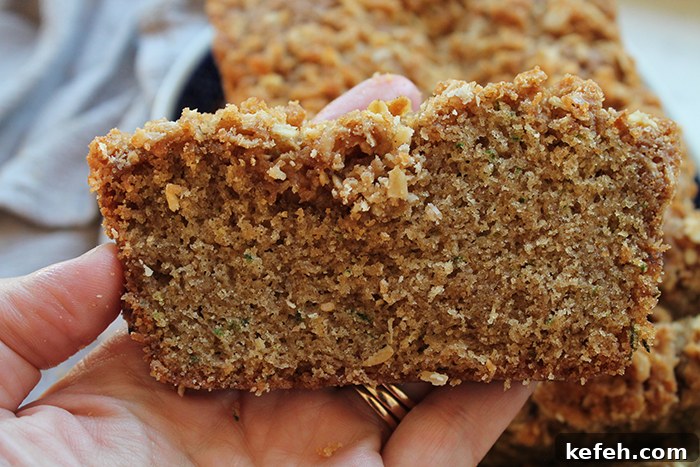 A slice of zucchini bread with streusel held above a loaf of zucchini bread.