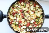 A large frying pan filled with slice zucchini and yellow squash, Italian sausage and dice tomatoes.