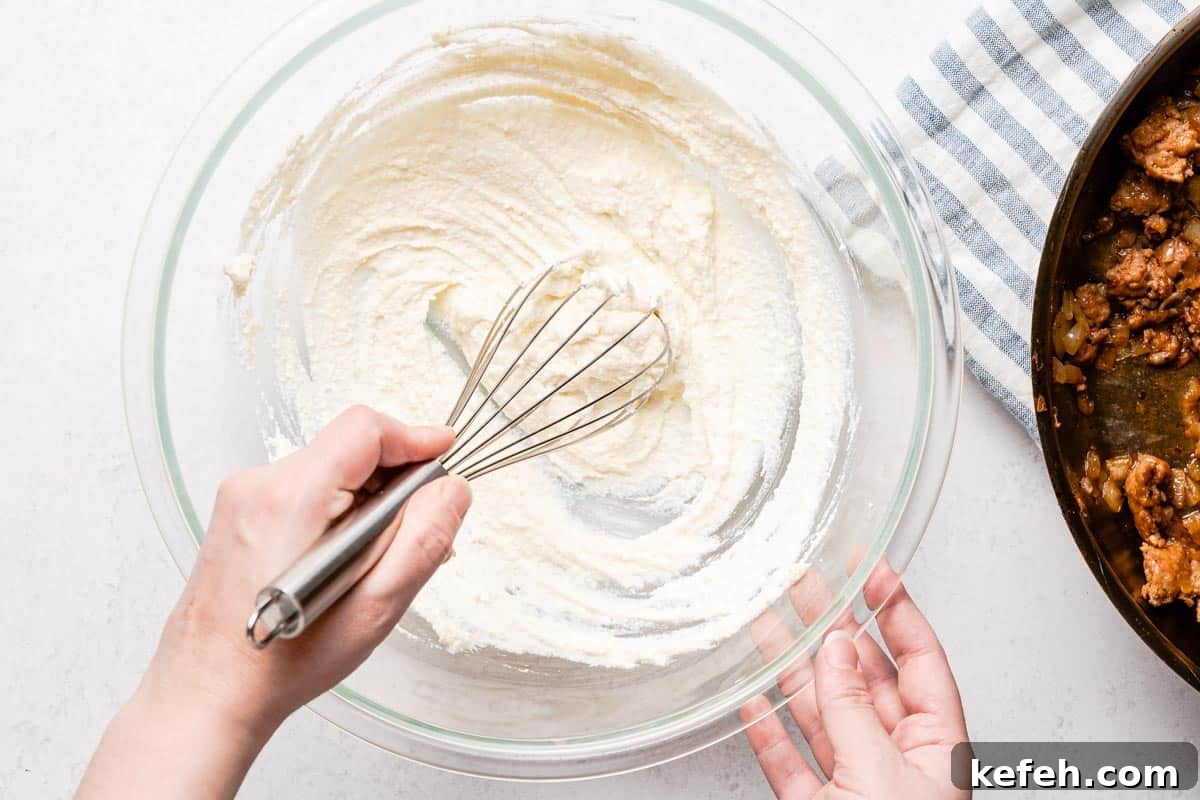 ricotta being whisked in large bowl with cooked sausage in pan on the side