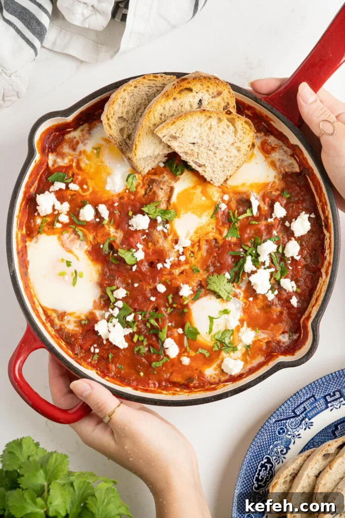 two hands holding shakshuka in a pan on a white counter