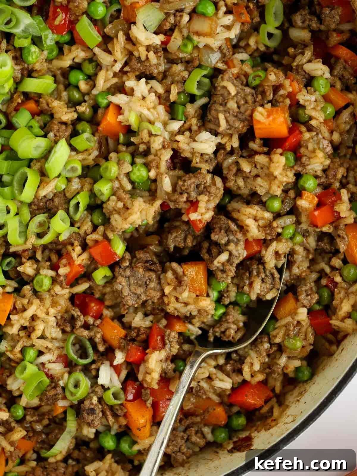 A close up of rice, beef and vegetables mixed together with a spoon ready to serve.