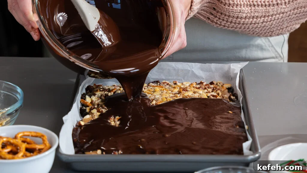Chocolate Bark with Dates, Pecans and Pretzels: Sweet & Salty Snack 5 Pouring chocolate on top of a cookie sheet filled with dates and peanut butter to make chocolate date bark.