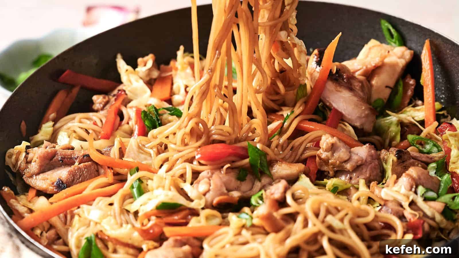 Stir-fried noodles with vegetables and chicken in a pan, featuring carrots, cabbage, and green onions.
